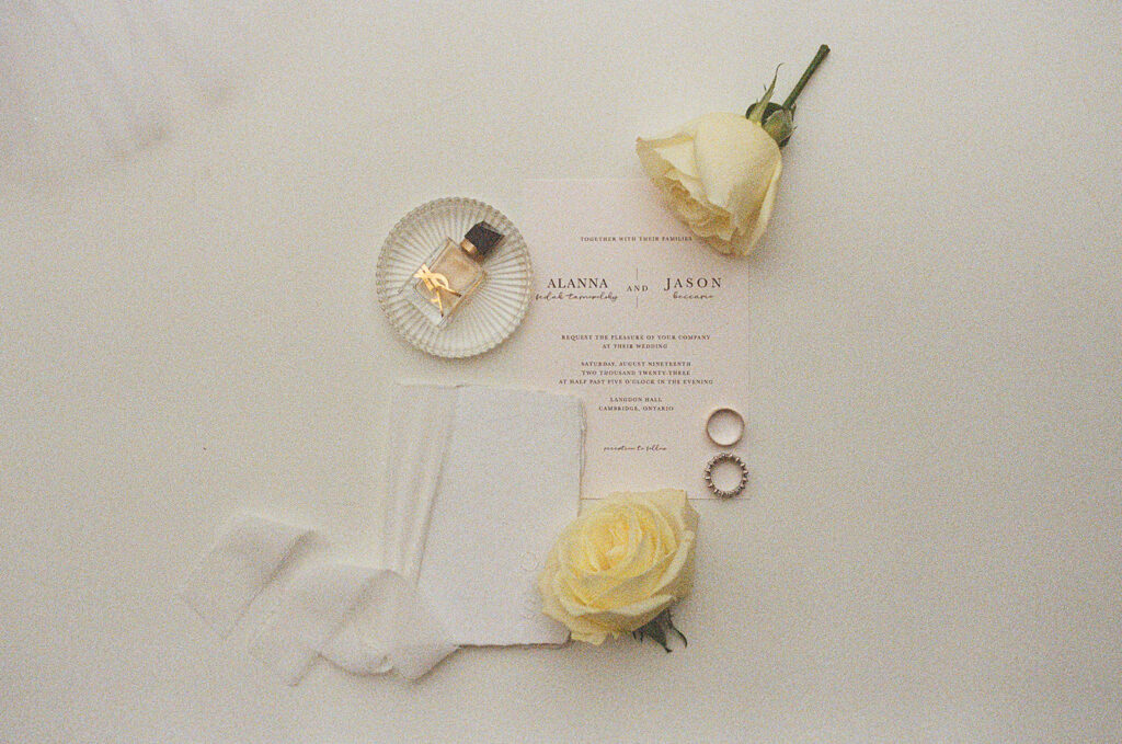 Wedding detail flat lay of an invitation, vow book, flowers and a ring dish with wedding rings and bands inside hybrid photography