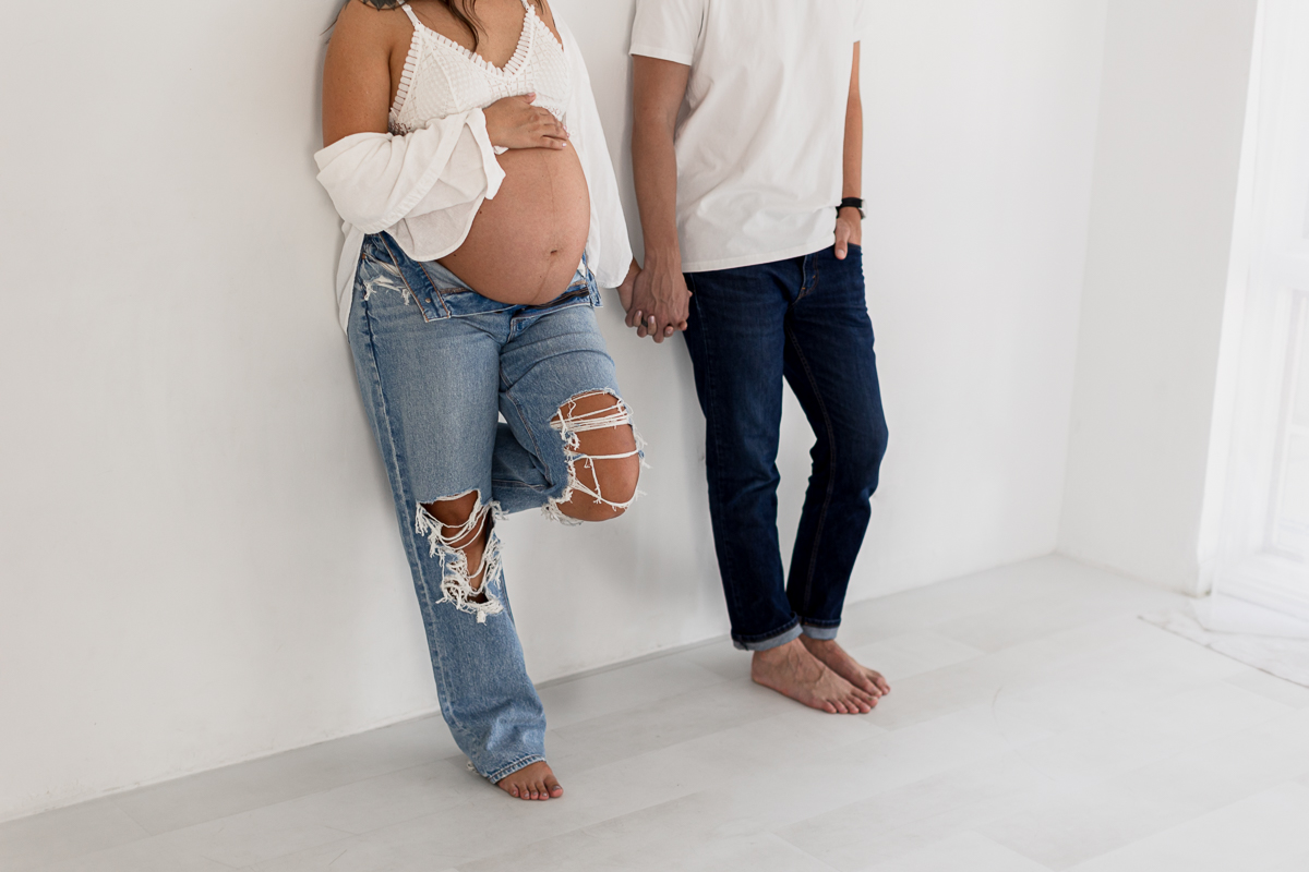 maternity photo of two people holding hands wearing denim and white shirts